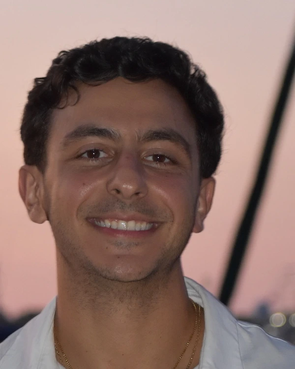 Alex Psichas smiling in a white shirt at sunset